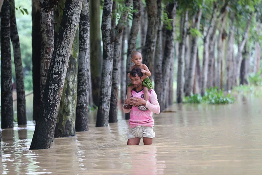 কোলের শিশুকে কাঁধে নিয়ে বন্যার পানি ভেঙে ত্রাণের খোঁজে যাচ্ছেন এক ব্যক্তি। জোগানিয়া কান্দাপাড়া, নালিতাবাড়ী
